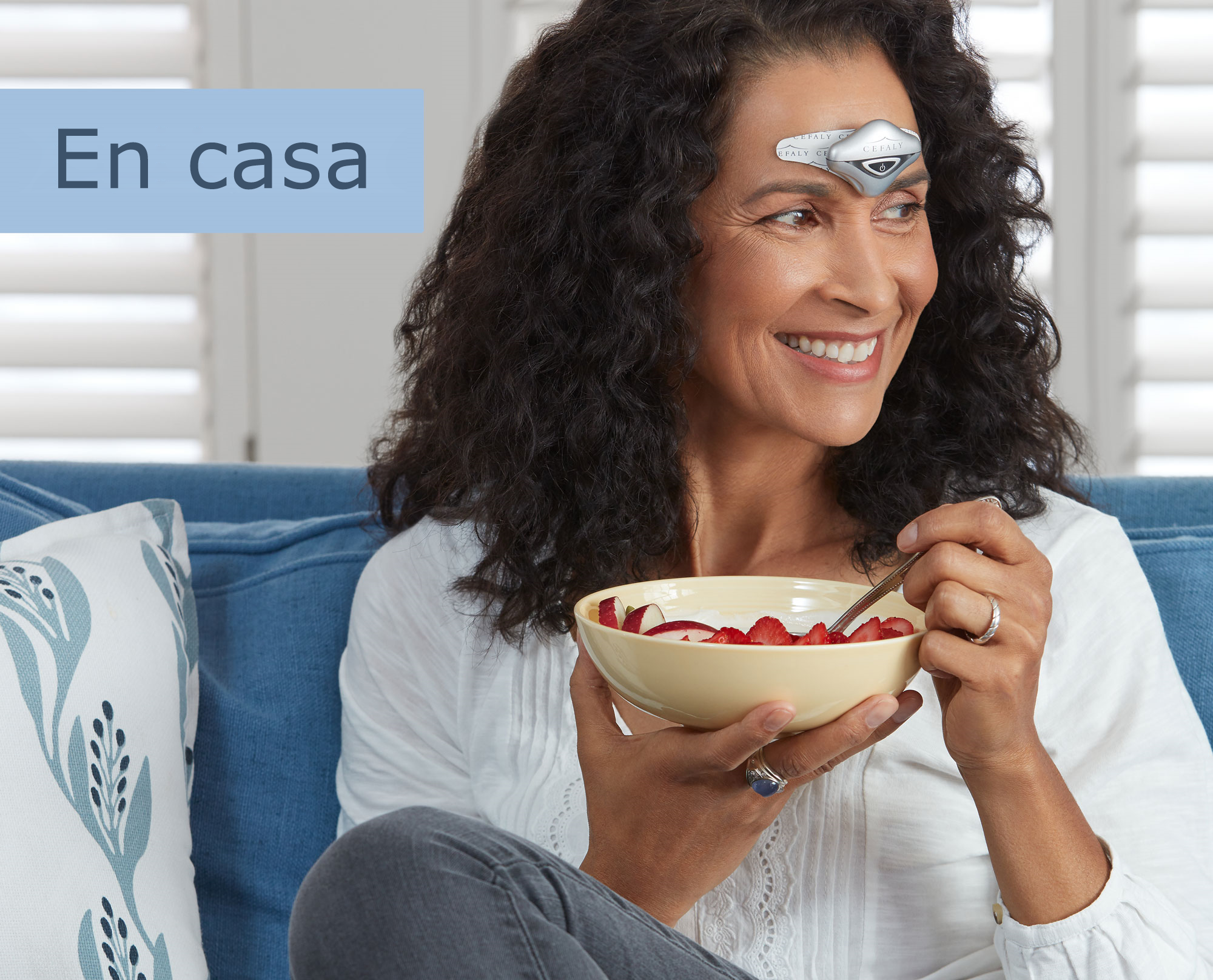 Mujer comiendo en un sofá mientras usa su dispositivo CEFALY para prevenir y tratar las migrañas